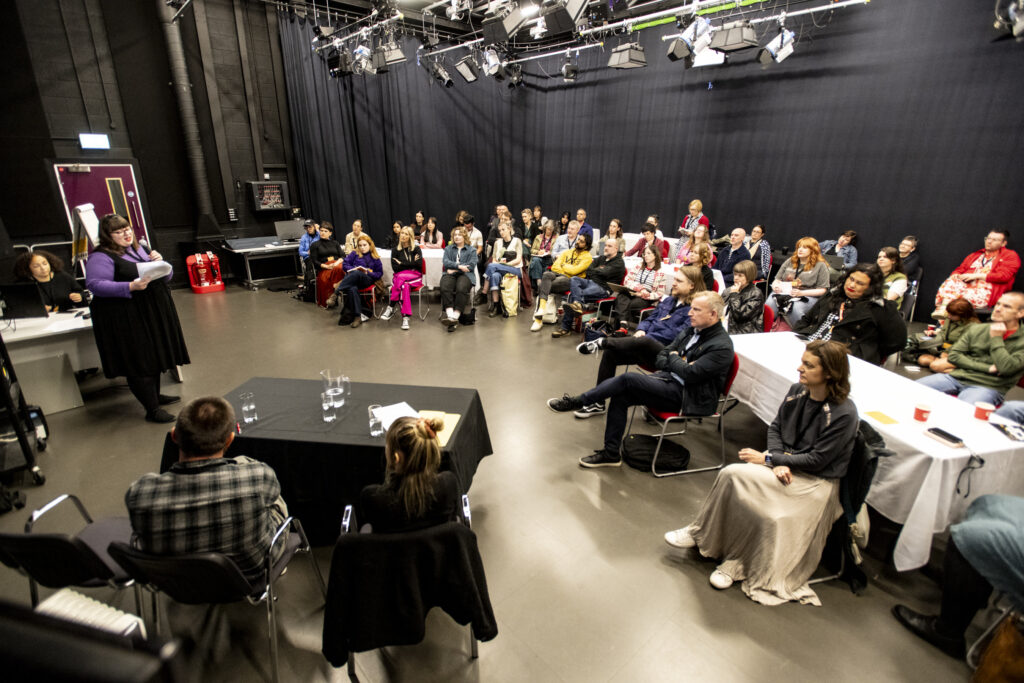 A crowd of people sitting and listening to a presenter